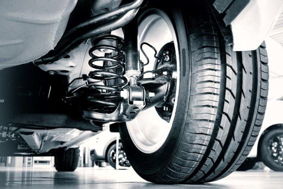 Close na suspensão automotiva com mola e amortecedor junto à roda, veículo elevado em oficina; imagem destaca qualidade e desempenho com peças da Suporte Distribuidora.